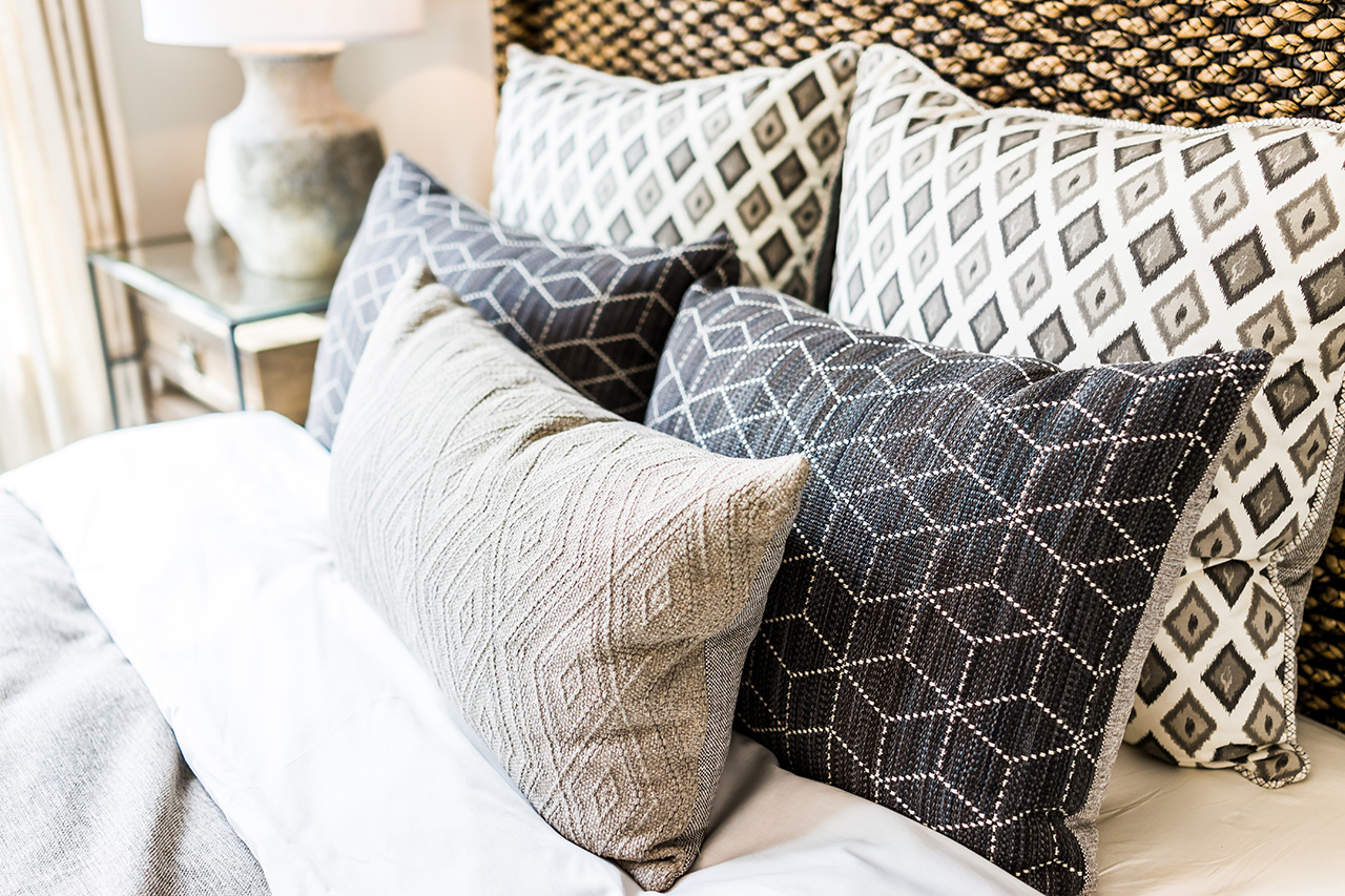 Closeup-of-new-bed-comforter-with-decorative-pillows,-headboard-in-bedroom-in-staging-model-home,-house-or-apartment
